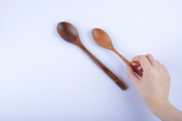 Mano femminile che tiene il cucchiaio di legno per la cucina su bianco.