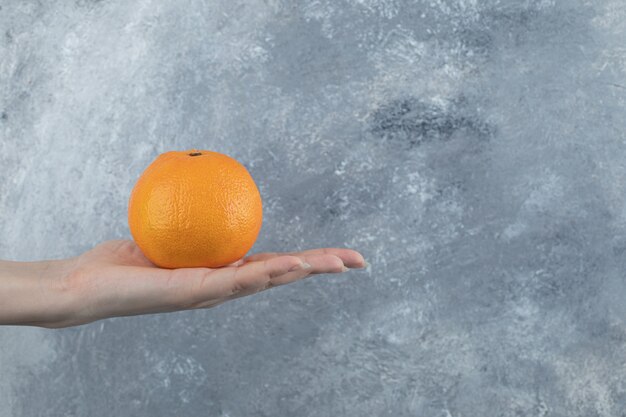 Mano femminile che tiene singola arancia sul tavolo di marmo.