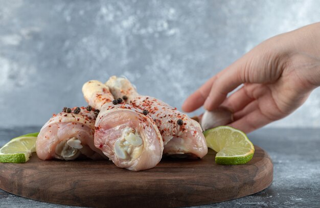 Mano femminile mettendo le fette di lime lato di cosce di pollo marinate su sfondo grigio.