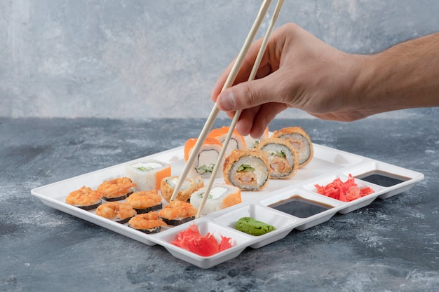 Mano maschio che prende il rotolo di sushi con le bacchette dal piatto bianco