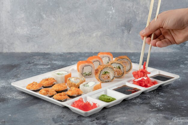 Mano maschio che prende il rotolo di sushi con le bacchette dal piatto bianco