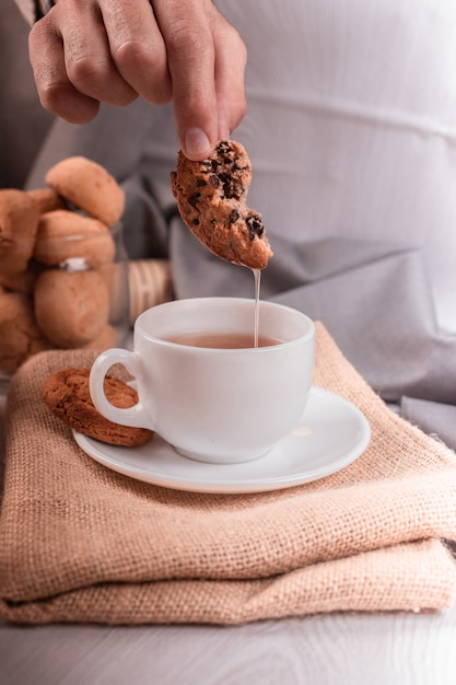 Mano maschio immergendo un biscotto al cioccolato nella tazza di tè