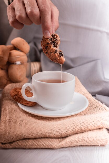 Mano maschio immergendo un biscotto al cioccolato nella tazza di tè