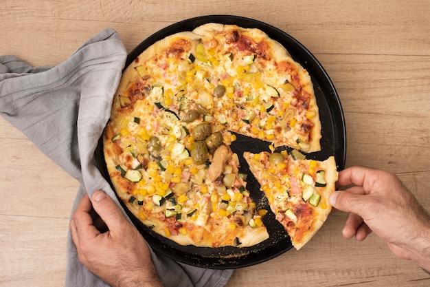 Mano piatta laici prendendo la fetta di pizza dalla padella con la pizza