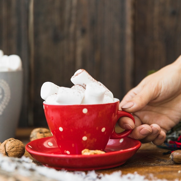 Mano umana che tiene tazza con marshmallow