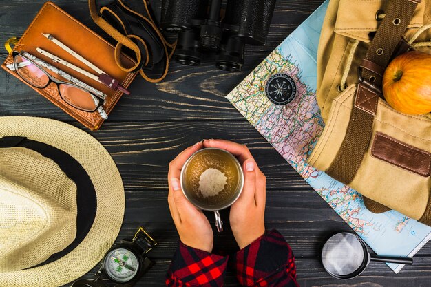 Mano umana che tiene tazza di caffè circondato con varie attrezzature di viaggio