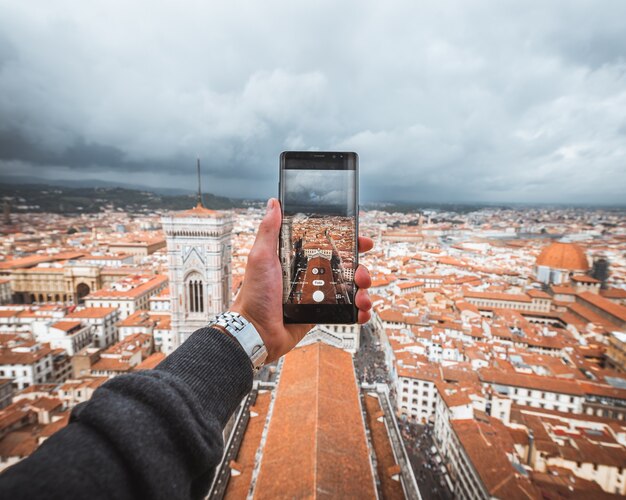 Mano umana che tiene uno smartphone per scattare una foto di Firenze