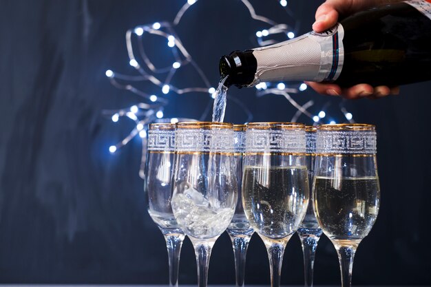 Mano umana versando champagne nel bicchiere trasparente alla festa