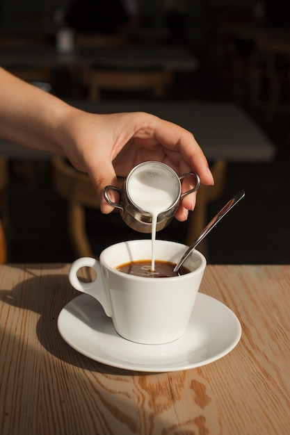Mano umana versando il latte nel caffè nero nella caffetteria