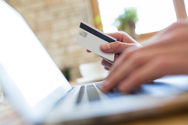 Mano usando un computer portatile per effettuare un pagamento online nel negozio di caffè