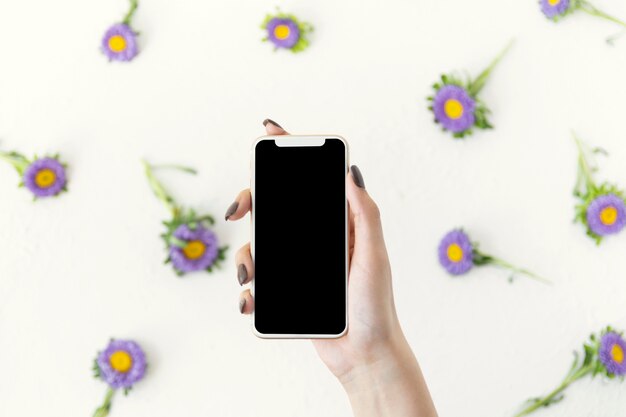 Mano vista dall'alto in possesso di un telefono circondato da fiori