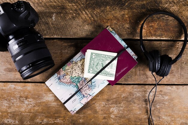 Mappa con passaporto, banconote, cuffia e fotocamera DSLR su superficie in legno