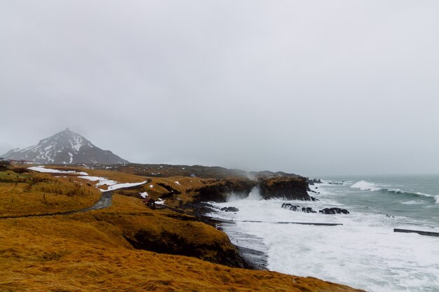 Mare mosso circondato da rocce coperte di neve ed erba sotto un cielo nuvoloso in Islanda