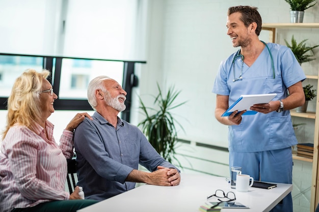 Marito e moglie maturi felici che parlano con il loro medico si attestano sui risultati dei test medici nel suo ufficio