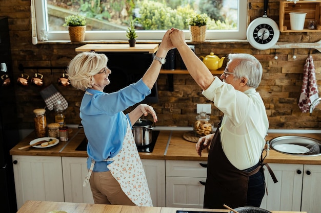 Marito e moglie maturi felici che si divertono mentre ballano in cucina
