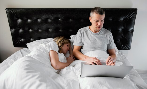 Marito utilizzando laptop mentre la moglie dorme