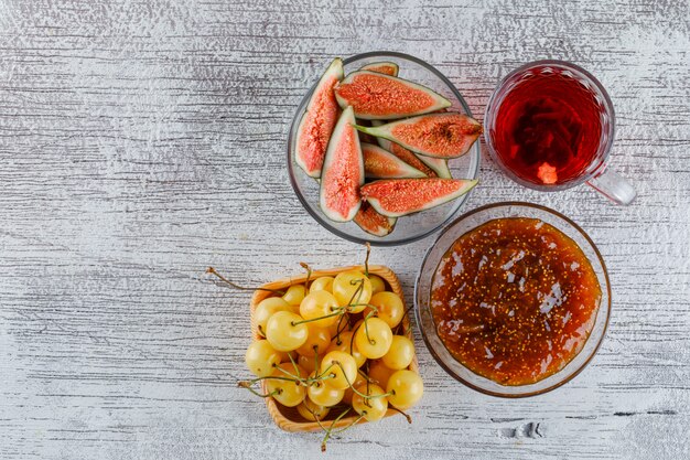 Marmellata di fichi con fichi, ciliegie, tazza di tè in una ciotola su sgangherata, vista dall'alto.