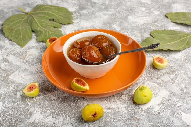 Marmellata di fichi dolci vista frontale con fichi freschi all'interno del piatto arancione sulla scrivania bianca