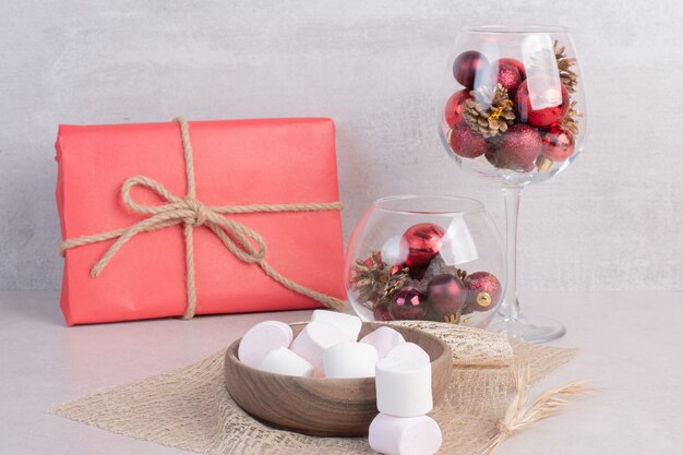 Marshmallow dolci sul piatto di legno con un bicchiere di palline rosse di Natale