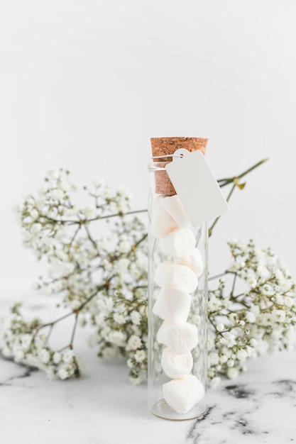 Marshmallow nella provetta con tag bianco e fiori bianchi su sfondo bianco