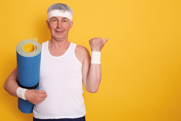 Maschera del maschio maggiore dai capelli bianco che posa nello studio isolato sopra giallo