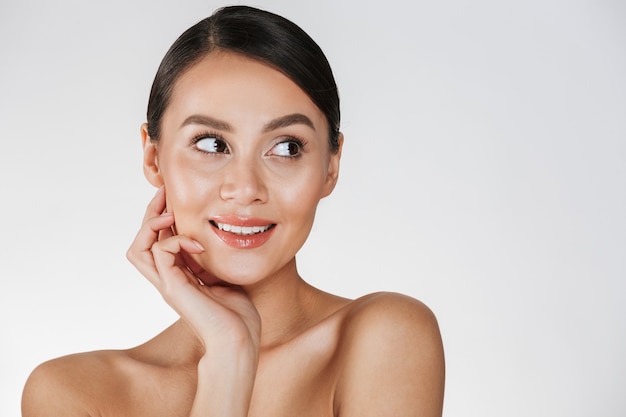 Maschera di bellezza della donna delicata con capelli marroni che osservano da parte e che tengono mano al suo fronte perfetto, isolato sopra bianco