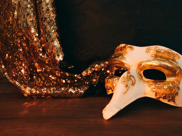 Maschera mascherata e tessuto dorato lucido con paillettes su scrivania in legno