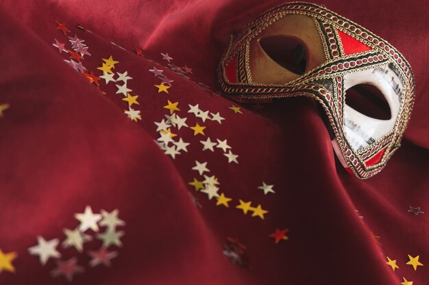 Maschera veneziana su un tessuto rosso con coriandoli stella