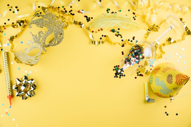 Mascherina della piuma di carnevale con il materiale della decorazione del partito e cappello del partito su fondo giallo
