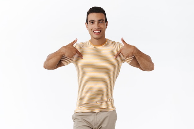 Maschile e fiducioso, felice ragazzo carino in t-shirt, che indica se stesso e sorride, disponibile aiuto