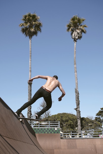 Maschio a torso nudo in sella a uno skateboard facendo un trucco all'aperto durante il giorno