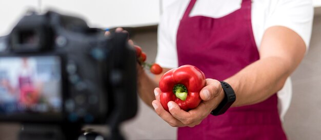 Maschio adulto del primo piano che presenta peperone dolce sulla macchina fotografica