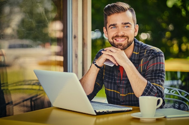 Maschio barbuto bello dei pantaloni a vita bassa che utilizza il computer portatile in un caffè.