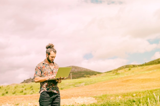 Maschio barbuto che lavora al computer portatile in campagna