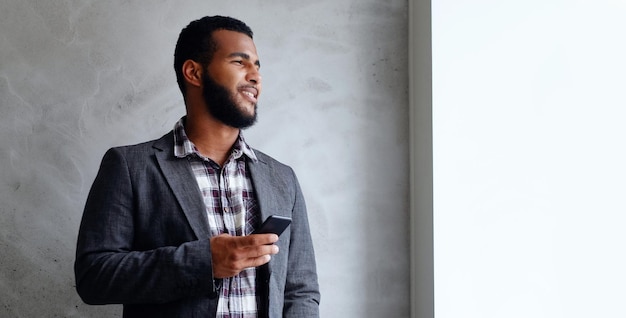 Maschio barbuto nero vestito con una camicia in pile e una giacca utilizzando uno smartphone.