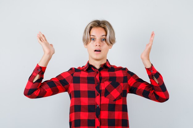 Maschio biondo teenager che finge di tenere qualcosa in camicia casual e sembra perplesso, vista frontale.