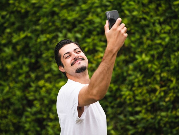 Maschio brunetta che si fa i selfie contro una vegetazione