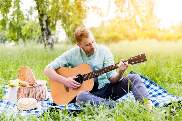 Maschio che gioca chitarra sul picnic in estate