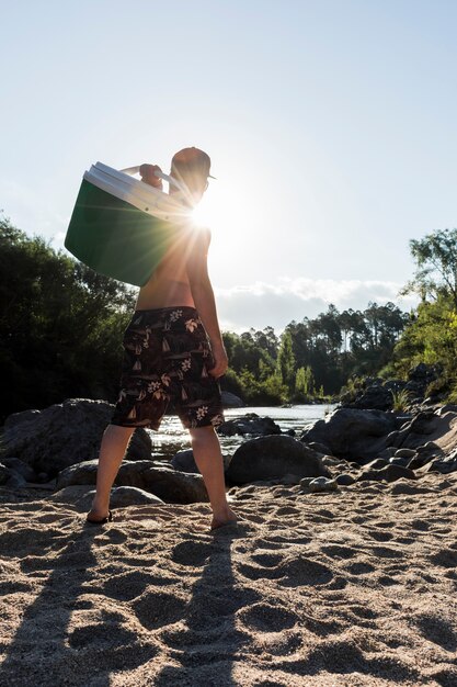 Maschio con la scatola fresca sulla costa di sabbia vicino al fiume