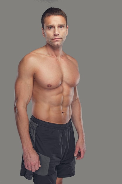 Maschio di mezza età abbronzato muscolare senza camicia isolato su sfondo grigio.