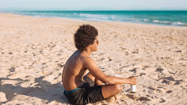 Maschio etnico che si siede sulla spiaggia che tiene birra