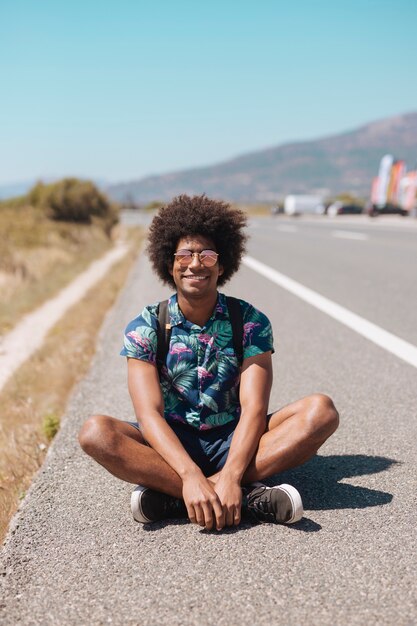 Maschio etnico sorridente che si siede sulla strada