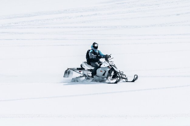 Maschio in sella a una motoslitta in un grande campo nevoso
