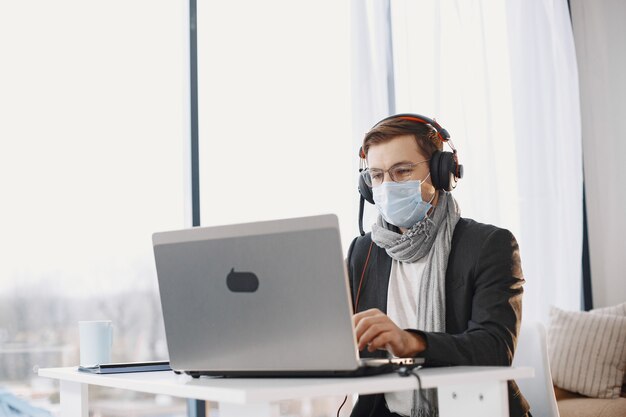 Maschio in una maschera medica. Uomo seduto nel soggiorno di casa. Ragazzo che si diverte a studiare in quarantena.