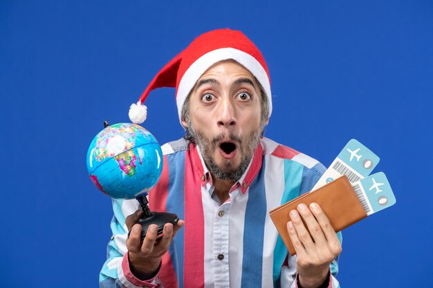 Maschio regolare di vista frontale con globo e biglietti sul nuovo anno di vacanze di emozione della parete blu