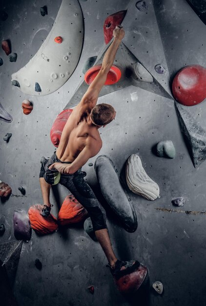 Maschio sportivo senza camicia che si arrampica su una parete da arrampicata indoor.