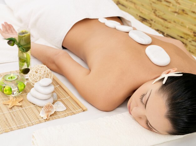 Massaggio con pietre per giovane donna al salone di bellezza spa. Terapia ricreativa.