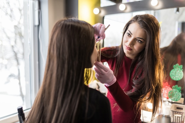 Master in guanti bianchi facendo trucco professionale di giovane donna