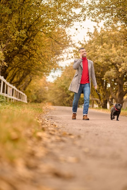 Mattinata al parco. Uomo che fa una passeggiata mattutina con un cane e parla al telefono