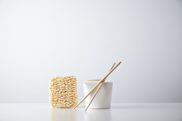 Mattone di spaghetti giapponesi secchi presentati vicino alla scatola da asporto al dettaglio blant chiusa con bacchette